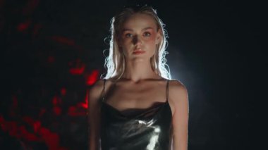 Projektör ışığı pozu veren güzel bir kadın uzaklaşır. Siyah arka planda parti gümüşü giyen seksi kız. Çekici, baştan çıkarıcı, sarışın, kameraya benzeyen, geceleri saçlarına dokunan. Profesyonel ateşli model çekimi. 