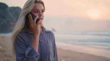 Deniz kıyısındaki kız akşam vakti cep telefonuyla konuşuyor. Deniz uçurumunda güzel bir gün batımı. Huzurlu, gülümseyen bir kadın tatilde akıllı telefonu arıyor. Güzel sarışın okyanus kıyısına gidiyor..