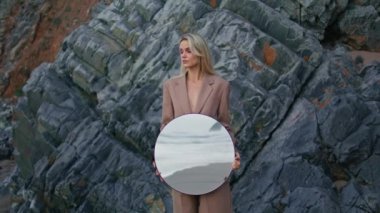 Sahildeki kız kayaları yakınlaştırıyor. Okyanus dalgalarının yansımasıyla ayna tutan çekici bir kadın. Plaj kayalığındaki profesyonel model kameralar. Sanat performansı konsepti