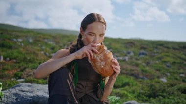 Sahada taze ekmek ısıran bir kız. Aç gezgin yaz pikniğinde yeşil tepenin tadını çıkarıyor. Moda mankeni güneş ışığında lezzetli yiyecekler yiyor. Hamur işi reklamı.