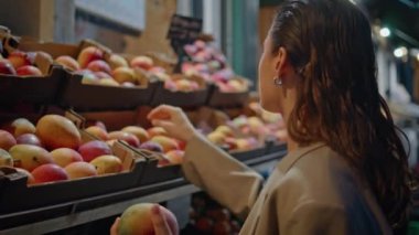 Kız akşamları marketten taze meyve topluyor. Vitamin yiyeceği seçen çekici bir kadın markette olgun elmaları kokluyor. Zarif bir bayan alışverişte bulunuyor..