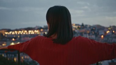 Esmer kadın aydınlanmış şehir manzarasına bakıyor. Gözetleme güvertesinde dikiliyor. Romantik kız, akşam kasabasının önünde korkuluk başında birini bekliyor. Genç bayan alacakaranlıkta kameraya poz veriyor.