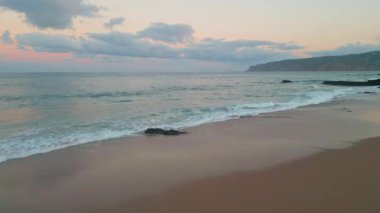 Sakin okyanus manzaralı hava manzarası. Alacakaranlık boyası ufku pembe gözlüklerle. Gün batımında sakin kumsalda hafif dalgalar dolaşır. Huzurlu bir gece kıyısı insansız hava aracı atışı. Pastel panoramik deniz kıyısı.