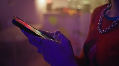 Kadın, Neon Club Parıltısı 'nda akıllı telefondan mesaj atıyor. Gece kulübünde arkadaşça buluşmayı beklerken cep telefonuyla mesajlaşan tanınmamış parti kızı. Genç kadın parmakları gece telefon ekranında yazı yazıyor..