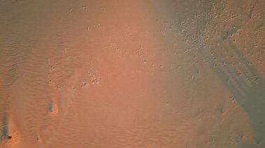 Gün batımında desenli kum tepeciklerini aşan hava manzaralı kum ayak izleri. Turuncu alacakaranlık ışıklarıyla yıkanan manzara dingin keşifler için geniş bir alan sunuyor. Doğa örnekleri, el değmemiş huzur dolu vahşi doğayı ortaya çıkarıyor.