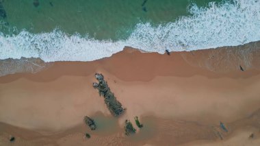 Köpüklü dalgalar sahili havadan seyrediyor. Turkuaz okyanus, kuma oyma dokusu. Sakin okyanus, dinamik kıyı manzarasıyla çelişiyor. Karayla deniz arasındaki barışçıl dalgalı sınırın insansız hava aracı çekimi..