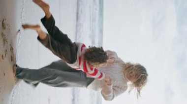 Neşeli anne okyanus kıyısında oğlunu döndürüyor. Mutlu bir aile, sonbahar tatili manzarasında okyanus sahilinde birlikte rahatlıyor. Güzel gülümseyen bebek bakıcısı kıvırcık çocukla eğleniyor.