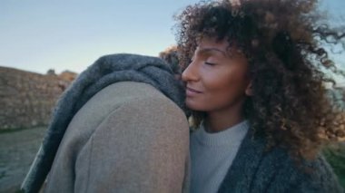 Deniz kıyısında sevgilisine sarılan mutlu bir kadın. Rahatlamış etnik insanlar birlikte eğleniyor. Sevgili çift rüzgârlı doğada sarılıyor.