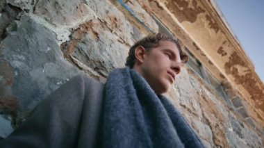 Eski binanın arka planında tek başına düşünen düşünceli bir model. Sonbahar paltosu ve atkısı içindeki üzgün adam mesafeyi düşünüyor.