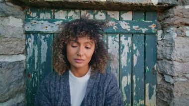 Rüzgarlı bir günde kıvırcık model poz veren duvar. Şehvetli, çekici bir kadın eski kapının önünde boyası soyulan kameraya bakıyor. Üzgün bronzlaşmış kız.