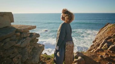 Kıvırcık kadın rüzgârlı sahilde okyanusa yakınlaşmayı düşünüyor. Bronzlaşmış hassas model, fırtınalı uçuruma bakıyor. Romantik kız denizi izliyor.