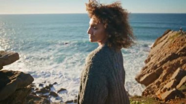 Güneşli bir günde uçurumun kenarında yürüyen bir kız. Bahar tatilinin tadını çıkaran mutlu turistler. Okyanusa hayran güzel bir gezgin.