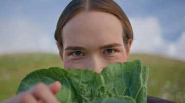 Sahada lahanayı yakından inceleyen bir kız. Yüzüne marul tutarak yeşil mutfak malzemelerini inceleyen portre kadını. Çiftlik sebzeleriyle mutlu vejetaryen görünümlü kamera. Organik gıda diyeti konsepti