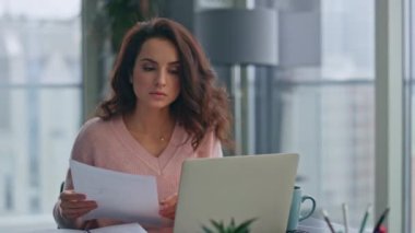 Patroniçe 'nin elinde evrakları tutarak ev ofisindeki bilgileri kontrol etmesi. Kendine güvenen güzel bayan yönetici bilgisayar okuma raporunda çalışıyor. Başarılı iş kadını uzak bir yerde oturuyor. 