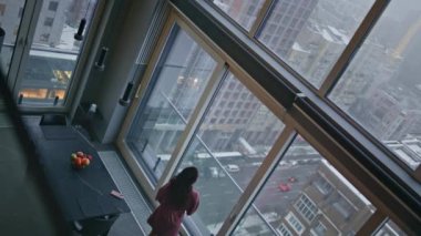 Ev kadını, çağdaş düz açılı yüksek açı çekiminde geleceğin panoramik penceresini düşünüyor. Düşünceli esmer ev hanımı şehir manzarasını seyrediyor. Zarif bayan kasvetli şehri izliyor. 