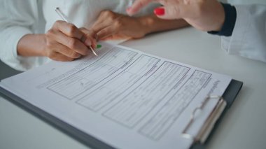 Sağlık hizmetleri kliniğinde yakın çekim hasta yazma formu. Kadın el işareti belgesi başvuruda yardımcı oluyor. Bilinmeyen Afro-Amerikan ziyaretçi hastane imzalama anlaşması. Tıbbi hemşire müşteriye yardım ediyor.