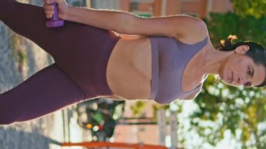 Sağlıklı kadın dambılları eğitiyor. Bir bacağı Sunshine Sokağı spor salonunda dikey çekimde. Ağırlık tutan aktif bir bayan dışarıda antrenman yapıyor. Sağlıklı sporcu kadın spor yapmaya çalışıyor.