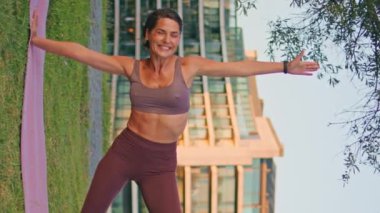 Gün batımı parkında dikey duran gülümseyen kadın. Dışarıda yoga yapan mutlu atletik bayan gülüyor. Sporcu kadın yaz aylarında kendini aktif hissediyor. Sağlıklı yaşam tarzı kavramı 