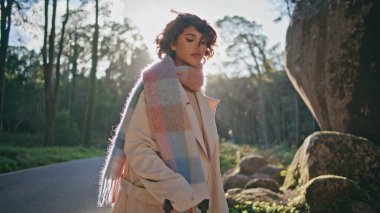 Şık bir turist, ormanın güneş ışığına poz veriyor. Yakından giyinmiş. Şık bir kadın, güneşli orman yolunda duran şık bir yolculuğu somutlaştırıyor. Moda gezgini seyahatte manzaralı rotayı keşfediyor..