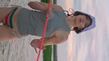 Akşamları rahatça nehir kıyısında balık tutan rahat bir kız. Güzel formda bir kadın hafta sonu balık yakalar. Mayo giymiş, elinde kelebek ağıyla kameraya bakan ciddi bir balıkçı.