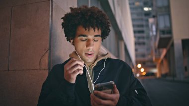 Sakin bir adam, şehir merkezinde kulaklık takarak akıllı telefonlardan konuşuyor. Kulaklıkla cep telefonuna bakan Latin kökenli genç bir adam. Kıvırcık öğrenci cep telefonu kullanıyor..