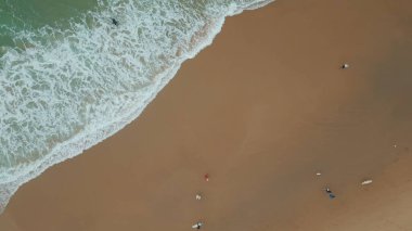 Sörfçüler köpüklü okyanus dalgalarının yanında kumlu kıyılarda yürür. Güzel köpüklü deniz suyu tropik plajları çok yavaş çekimde yıkıyor. Çeşitli sörfçüler yaz tatilinde spor hobisinin keyfini çıkarıyorlar..