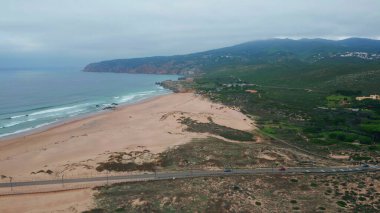 Kumsalın kenarları engebeli kıyı şeridi ve okyanus dalgaları. Güzel deniz suyuyla yıkanmış, köpüklü hava manzaralı deniz manzarası. Güçlü dalgalar bulutlu kıyı şeridine yuvarlanıyor yemyeşil yemyeşil