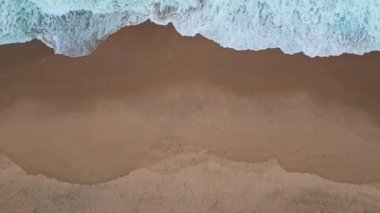 Köpüklü dalgalar, boş kıyı şeridi hava manzarası. Muhteşem turkuaz deniz manzaralı doğa gücü süper yavaş çekimde güzel kıyılara sıçrıyor. Mavi deniz suyu plajı yıkıyor. Huzurlu deniz manzarası