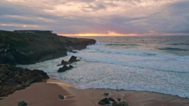 Okyanus dalgaları üzerinde gün batımı. Kıyı kayalıkları üzerindeki insansız hava aracı vuruşu. Akşamları kayalık kıyılarda su sıçrayan güzel deniz köpüğü çok yavaş bir şekilde parıldıyor. Yaz günbatımında sakin deniz manzarası.