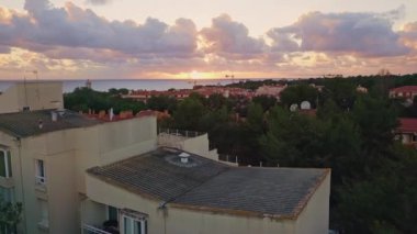 Sahil kasabası akşam güneşini aydınlatıyor. Çatılardan panoramik manzara sakin deniz ufkunu vurguluyor. Konut cazibesiyle okyanus manzaralarını birleştiren manzaralı bir gökyüzü. İnsansız hava aracı manzaralı çatı evleri çekti.