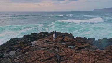 Okyanus kıyısında dalgaları izleyen yalnız bir kadın. Kâşif, alacakaranlık drone atışında huzurlu deniz manzarasının tadını çıkarıyor. Turkuaz deniz manzarası ve büyüleyici gökyüzü gezgini. Deniz manzarası.