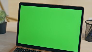 Modern yeşil ekran laptop ofis masasına yakın plan yerleştirilmiş. Açılan dizüstü bilgisayarın görüntüsü yeşil ekran monitörü şirket işi için hazır. Açık şirket işyerinde boş krom anahtar bilgisayar görüntüsü
