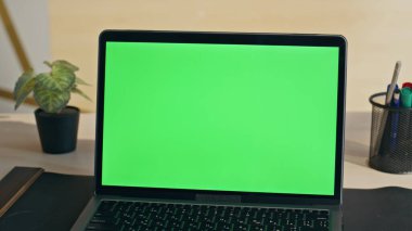 Şirketin iş yerinde boş krom anahtar dizüstü bilgisayar görüntüsü. Modern ofis masasında duran yeşil ekran bilgisayar monitörü. Masaya yerleştirilmiş şablon maketi defteri. İş akışı konseptinde teknoloji 