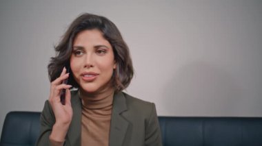 İş kadını ofisin iç kısımlarında akıllı telefon görüşmesi yapar. Modern koltukta oturarak cep telefonuyla iletişim kuran zarif bir yönetici portresi. Şirket kanepesinde cep telefonuyla konuşan gülümseyen kadın..
