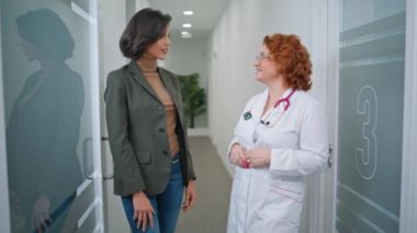 Gülümseyen sıhhiyeci modern klinikte hastaya müdahale ediyor. Kürk giyen neşeli bir profesyonel, poliklinik koridorunda sağlık görevlisiyle konuşuyor. Gülümseyen doktor kadın içeride esmerle tıbbi tavsiyelerini paylaşıyor..
