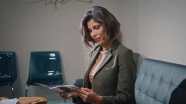 Şirket ziyaretçisi koltukta oturmuş moda dergisine yakından bakıyor. Kendine güvenen iş kadını ofis kanepesinde rahatlatıcı bir makale okuyor. İş ortamında iş görüşmesi bekleyen güzel bir kadın..