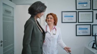 Gülümseyen doktor tıbbi muayenehanedeki hastaya hoş geldin diyor. Modern klinikte beyaz önlüklü, esmer bayanı selamlayan profesyonel bir doktor. Şık bir bayan hastanede sağlık hizmetleri randevusuna gidiyor..