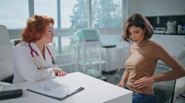 Klinikteki hasta, profesyonel doktorla konuşurken mide rahatsızlığı yaşıyor. Tıbbi konsültasyonda karın ağrısını açıklayan bir kadın. Bayan pratisyen doktor ziyaretçi sorunu yaşıyor.