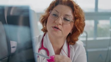 Sağlık uzmanı, klinikte detaylı açıklamalar sunan bir hastayla röntgen bulgularını tartışıyor. Tıbbi teşhisten bahseden yetenekli bir kadın doktor. Ciddi terapist imajı inceliyor