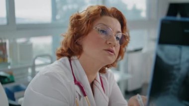 Tıbbi uzman, klinik randevusunda teşhis koyan röntgenleri inceliyor. Radyolog, sağlık hizmetleri konsültasyonunda inceleme sonuçlarını açıklıyor. Poliklinik hastasıyla konuşan profesyonel bir doktor..