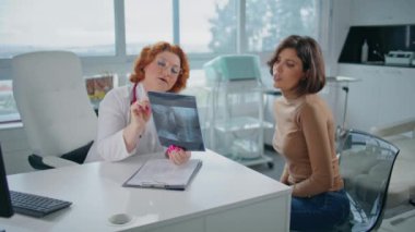 Sağlık uzmanı modern klinikteki hastaya röntgen filmini açıklıyor. Radyoloji analizi yapan profesyonel bir doktor teşhis görüntüsünü inceliyor. Tıbbi danışmanlık sağlayan ciddi bir terapist..