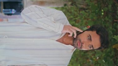 Akdeniz balkonunun dikey çekiminde akıllı telefondan konuşan seksi bir adam. Şehir bağında cep telefonundan konuşan yakışıklı bir adam. Bronzlaşmış esmer maço iletişim kuran cep telefonu yeşil yolda yürüyor.