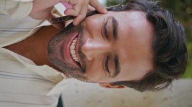 Şehrin arka sokağında dikey çekimde neşeli esmer konuşan akıllı telefon. Yakışıklı, mutlu bir adam cep telefonunu arıyor. Keyifli. Gülümseyen seksi maço cep telefonu görüşmesi parkta tek başına duruyor.