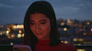 Cep telefonu kullanan neşeli bir bayan. Şehir merkezinde dinleniyor. Çekici, mutlu bir kadın elinde telefonla aydınlanmış kasaba geçmişinde modern uygulamalara göz atıyor. Pozitif esmer görünümlü cep telefonu ekranı