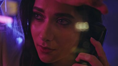 Neon Modeli gece hayatının tadını çıkarıyor. Çekici, rahat, dinlenen bir kız telefon kulübesi açık hava fotoğraflarına bakıyor. Moda, güzel esmer, elinde cep telefonu, tek başına cevap bekliyor.