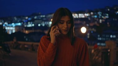 Kapanış gecesi kadını cep telefonunu arıyor. Şehir manzarası aydınlanmış. Açık havada akıllı telefondan konuşan kırmızı elbiseli nazik genç bayan. Geceleri cep telefonuyla konuşan romantik bir kadın.