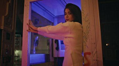 Baştan çıkarıcı kadın neon ışıklı portrede telefon kulübesi pozu veriyor. Mutlu şehvetli kadın kameraya bakıp gece yakın planda gülüyor. Rahatlamış gülümseyen manken tasasız bir akşam yaşıyor. Gece hayatı konsepti