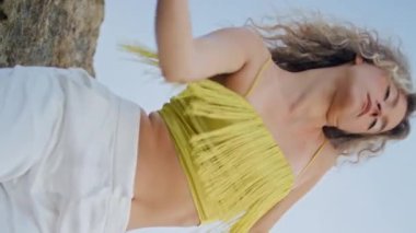Gökyüzüne karşı dans eden etkileyici kadın doğanın dikey video çekiminde koreografi yapıyor. Kıvırcık kız taşlı kayalarda şehvetle hareket ediyor. Kameraya bakıp düzgün hareketler yapan sarışın.