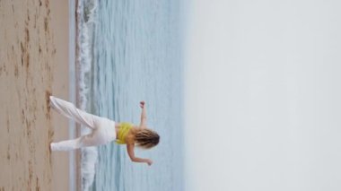 Esnek dansçı kız, akşam deniz kıyısında dikey görüntüde ince vücut bükme dansı yapıyor. Sahilde dans eden sanatçının koreografisi. Çağdaş tarzını icra eden muhteşem genç bir kadın..