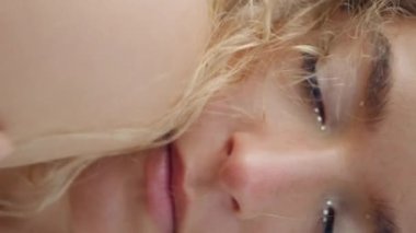 Dikey video yakın çekim kıvırcık kadın doğada poz veriyor. Omuz derisine elle dokunuyor. Açık havada parlak makyajlı romantik bir genç kızın portresi. Güzel sarışın kamera rahatlatıcı kumsal